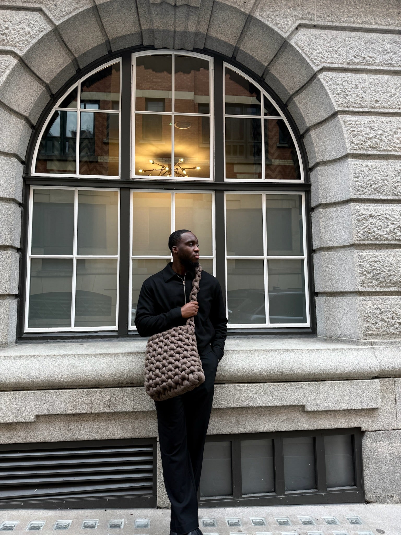 Man holding a textured bag in front of a stone building with large windows
