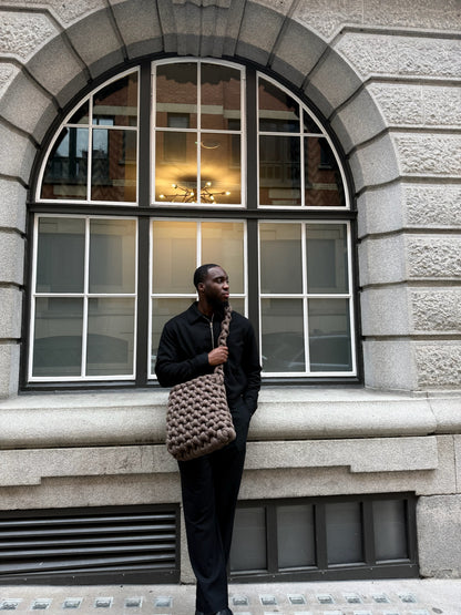 Man holding a textured bag in front of a stone building with large windows