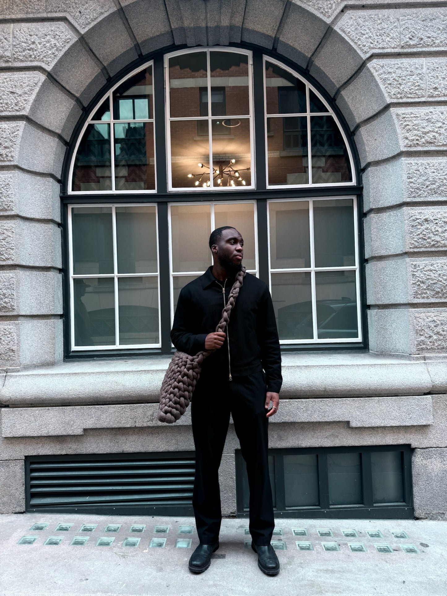 Man holding a patterned bag standing in front of a building with large windows.