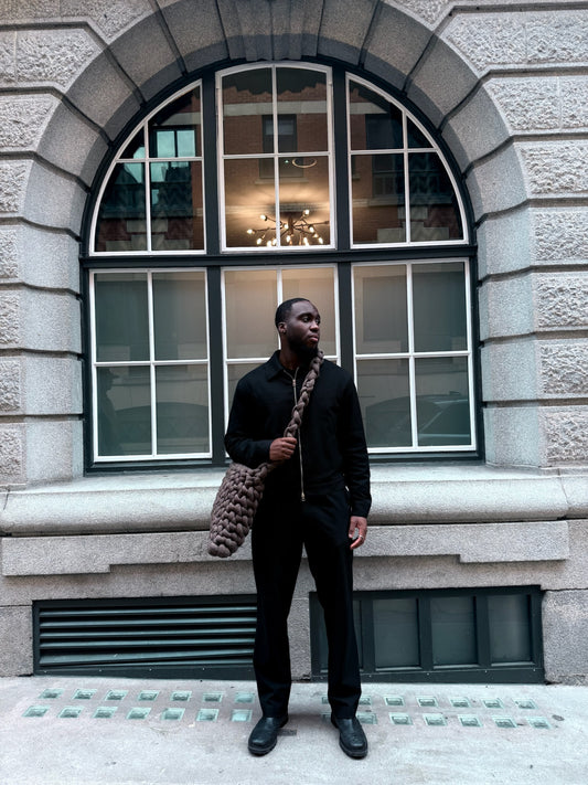 Man holding a patterned bag standing in front of a building with large windows.