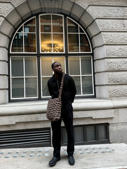 Person holding a textured bag in front of a stone building with large windows
