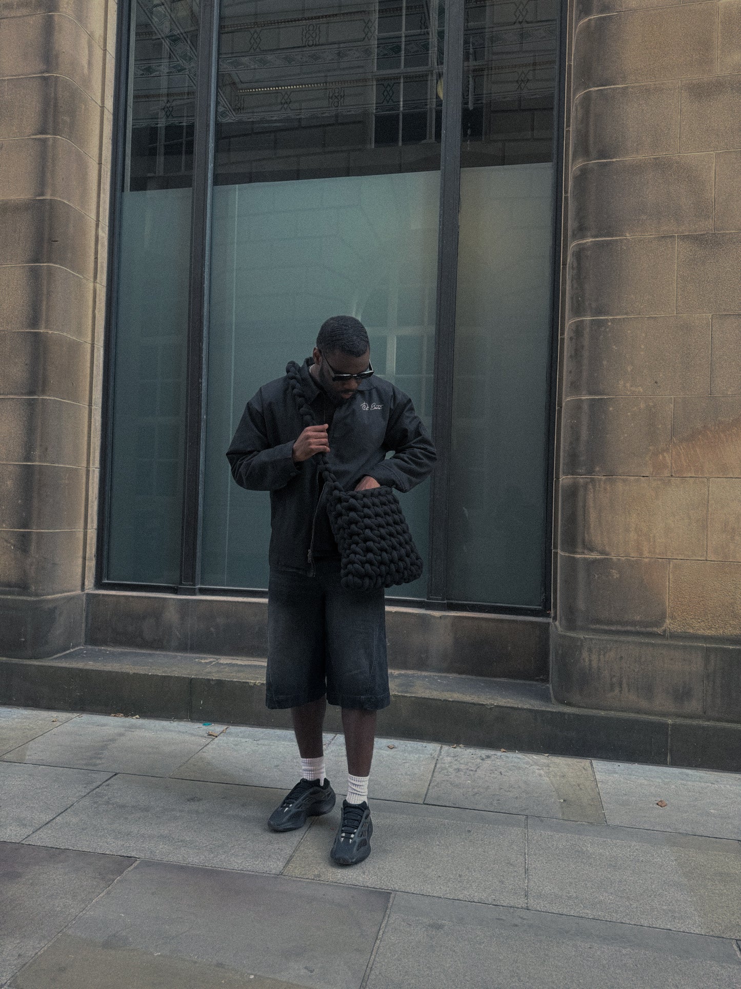 Person in dark clothing holding a textured bag against a building background