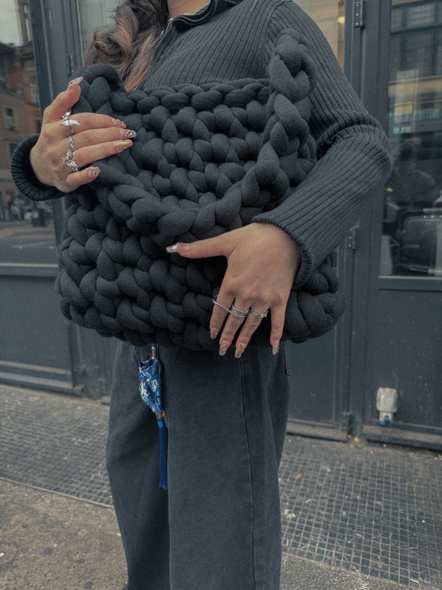 Person holding a large black knitted clutch in an urban setting