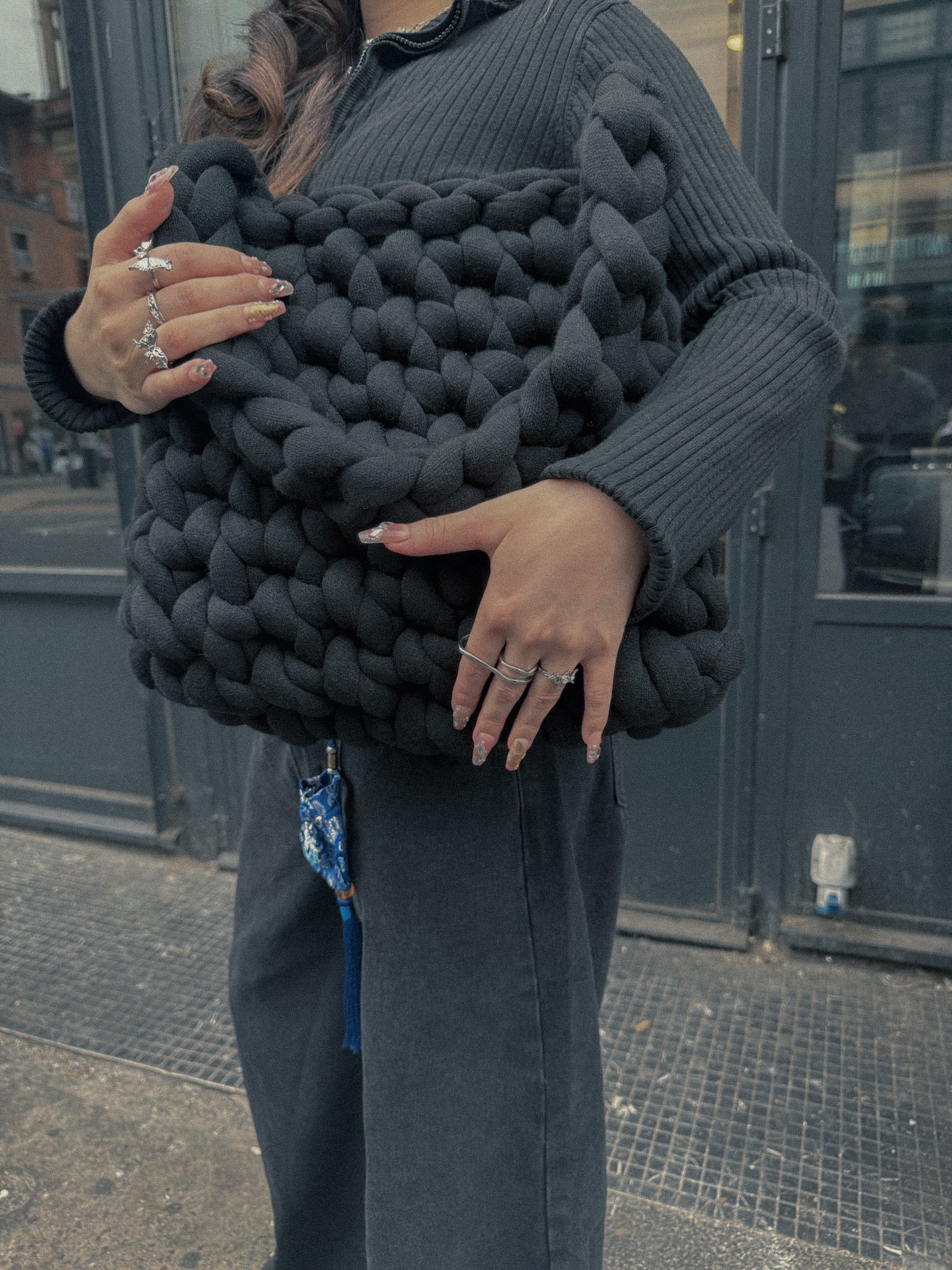 Person holding a large black knitted clutch in an urban setting