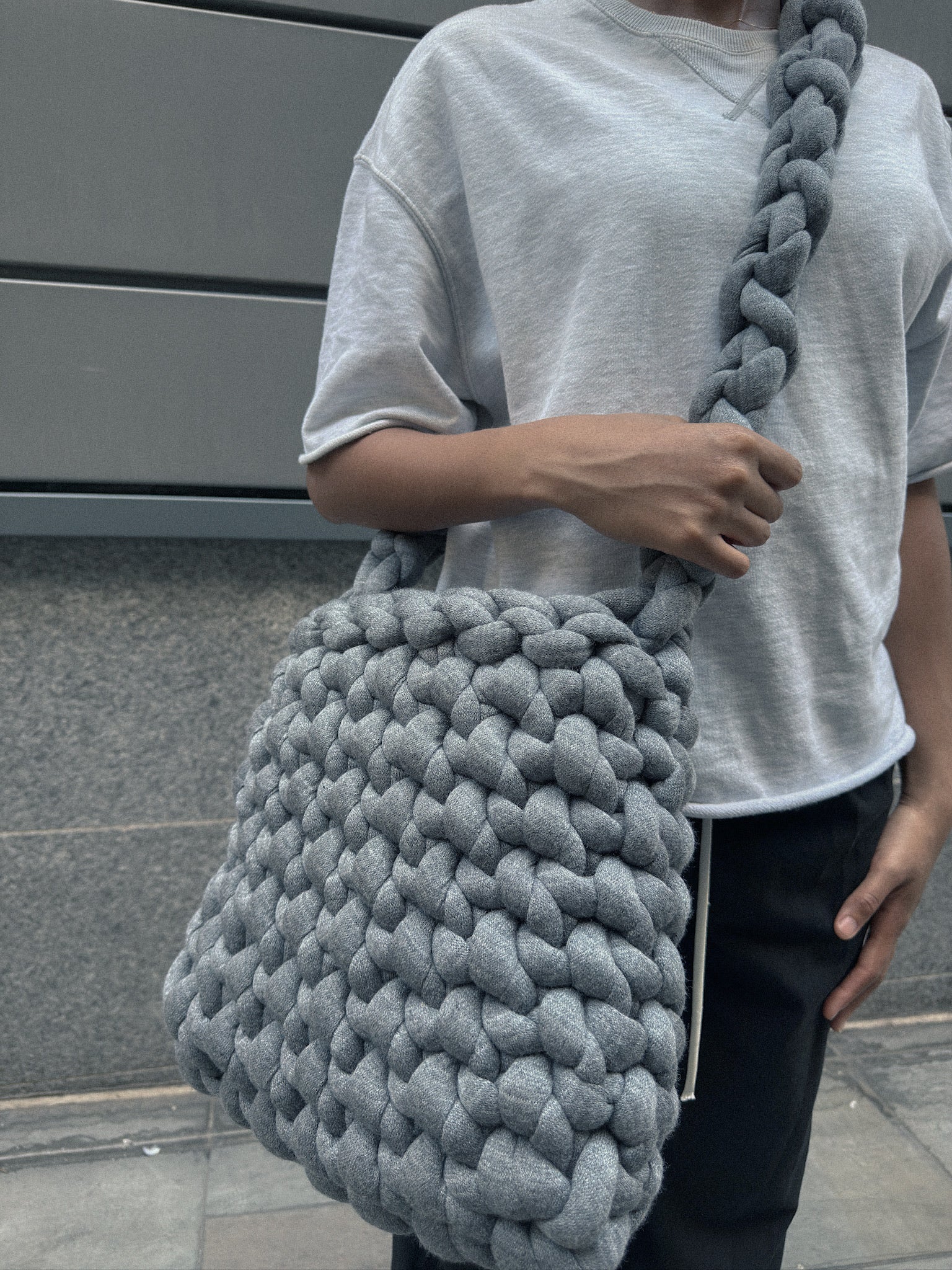 Person holding a large gray knitted bag against a neutral background
