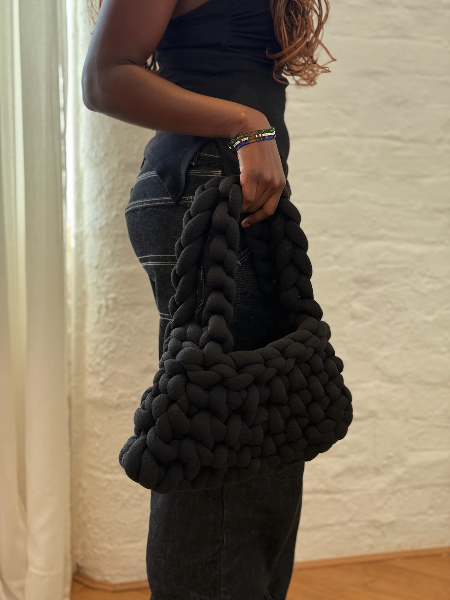 Person holding a large black knitted blanket against a neutral background